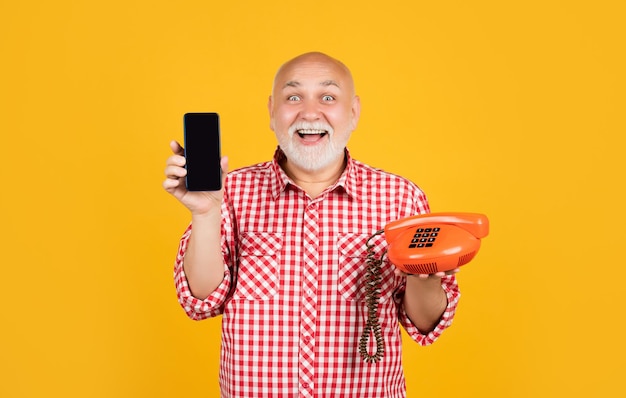 Un anciano alegre con un teléfono retro y un smartphone moderno con fondo amarillo