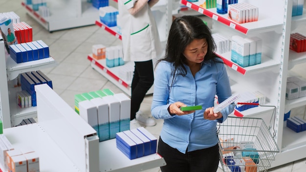 Foto anciano analizando cajas de medicamentos en la tienda de medicamentos, mirando productos farmacéuticos para el tratamiento de la salud. mujer asiática en farmacia revisando suministros médicos. disparo de mano.