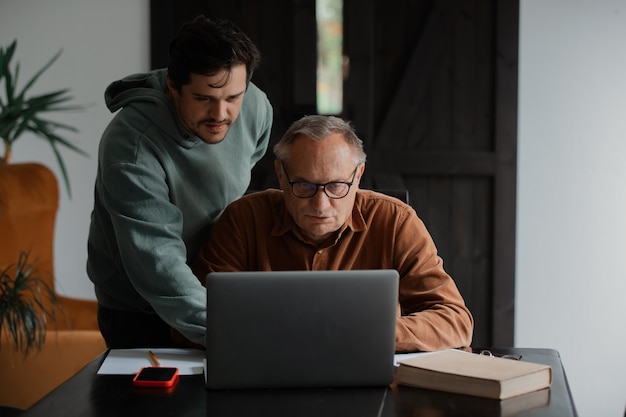 Anciano en anteojos y su hijo usando la computadora portátil en casa.