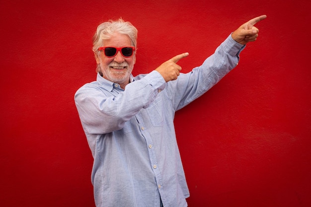 Un anciano apuesto de cabello blanco con camisa informal y anteojos sobre fondo rojo con una sonrisa feliz y fresca en la cara Persona afortunada gesticulando con las manos