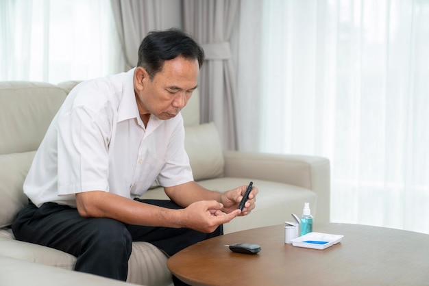 Foto anciano asiático comprobar un nivel de azúcar en la sangre por él mismo en casa para el control de la insulina la diabetes y el control de la salud en su dedo
