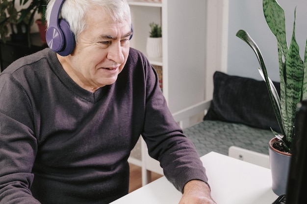 anciano, con, auriculares, sentado, en la mesa, canas, viejo, utilizar, computador portatil, trabajando, en, computadora