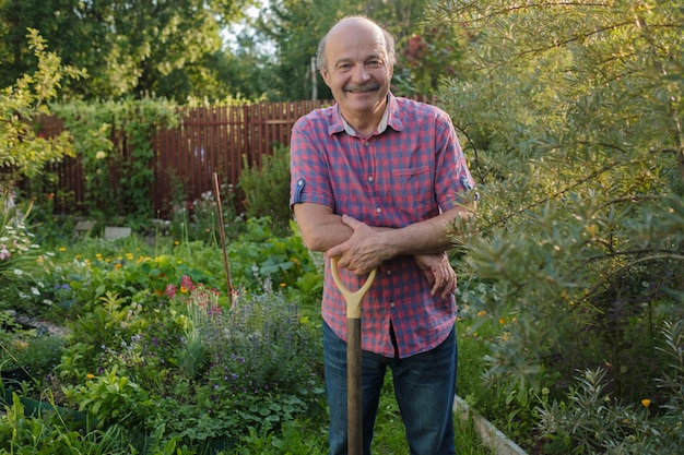 Anciano con un bigote de pie en el jardín de verano, sonriendo.