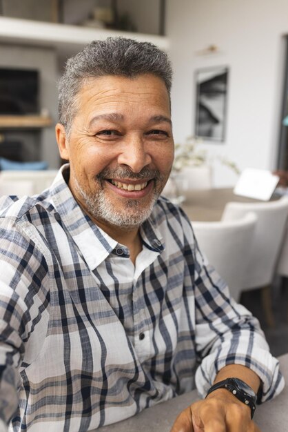 Foto un anciano biracial de cabello gris sonríe cálidamente en una llamada de video con una camisa a cuadros y un reloj