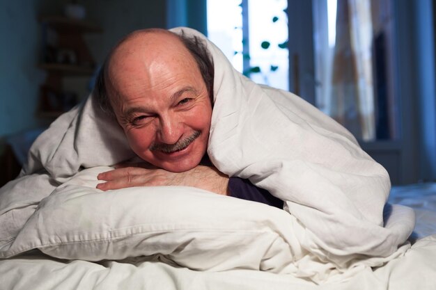 Un anciano calvo con bigote yace en la cama abrazando una almohada Tiene un problema con el sueño