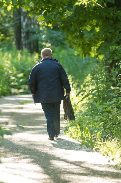 Un anciano caminando por el sendero en el bosque verde de verano