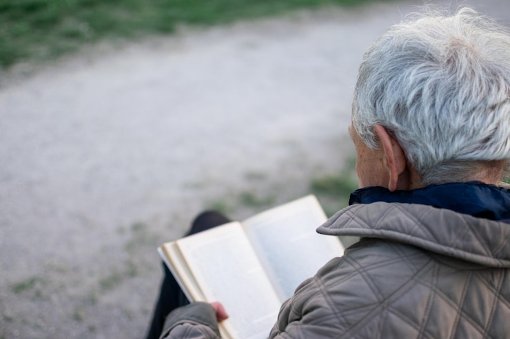 Anciano con canas leyendo un libro sentado en un banco