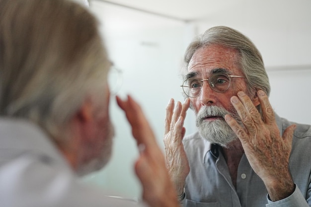 Anciano con canas revisando el cabello frente al espejo