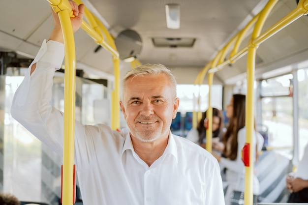 Un anciano canoso con una elegante camisa blanca se para en medio de un autobús