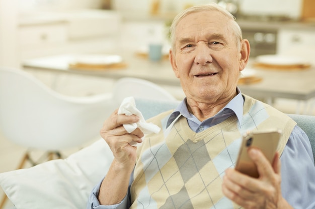 Anciano enfermo sentado en el sofá y sosteniendo un teléfono