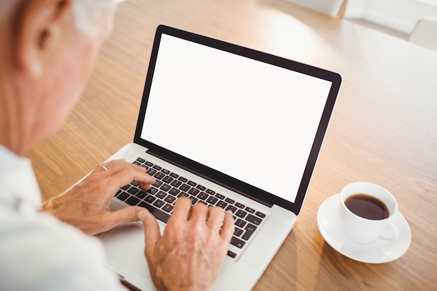 Anciano enfocado escribiendo en la computadora portátil en casa