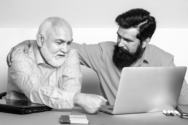 Un anciano enseñando una laptop a su hijo mayor y a su padre mayor usando la computadora juntos discutiendo noticias