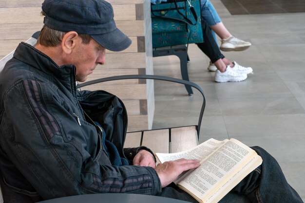 Un anciano está sentado en un banco y leyendo un libro Un hombre con un libro en sus manos descansa después del trabajo