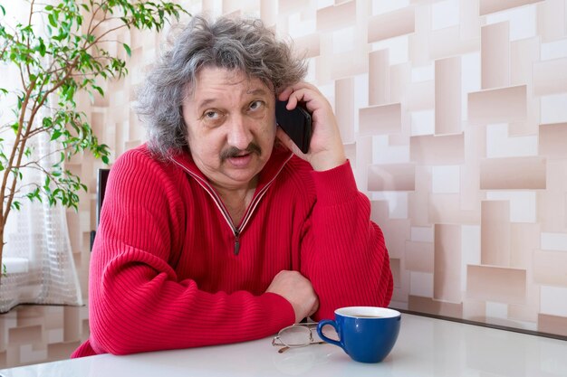 Un anciano está sentado a la mesa y hablando por teléfono.