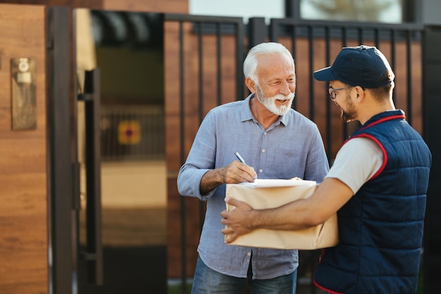 Un anciano feliz hablando con un mensajero mientras recibe su paquete en casa