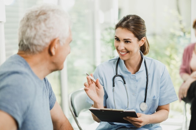 Un anciano feliz y su doctora comunicándose en la sala de espera de la clínica médica.