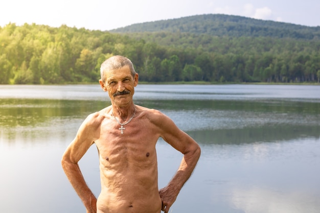 Anciano flaco con el torso desnudo en el fondo de un paisaje de un lago y un bosque