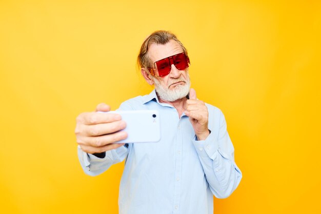 Anciano en gafas rojas de moda con un fondo de teléfono amarillo