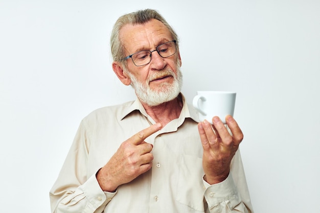 Anciano con gafas con una taza sobre un fondo blanco y una camisa blanca