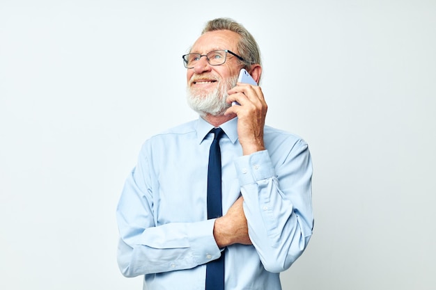 Un anciano con gafas con un teléfono en el estudio sobre un fondo blanco hablando