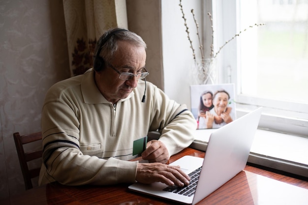 Anciano con gafas usando laptop en casa.