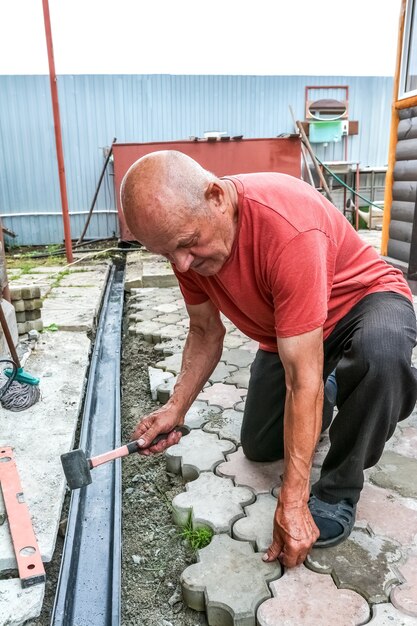 un anciano hace un camino peatonal con losas de pavimentación actividad laboral en la parcela del hogar