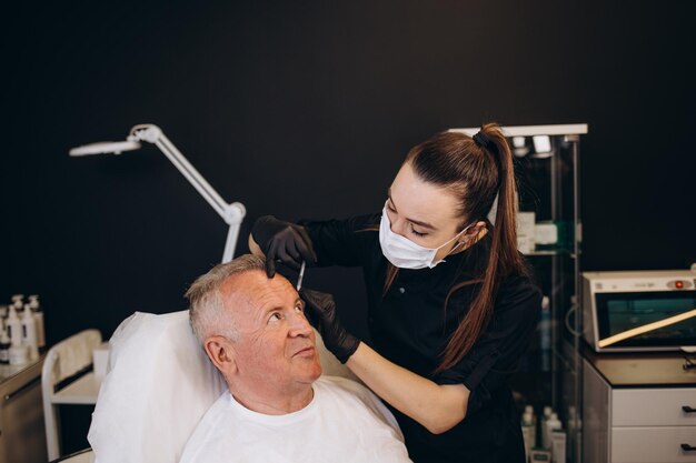 Un anciano hace una inyección para las arrugas en un salón de belleza