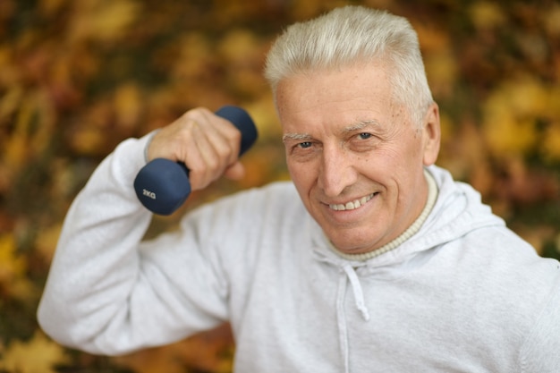 Anciano haciendo ejercicio con pesas en el parque otoño