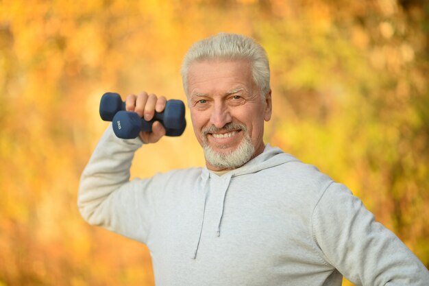 Anciano haciendo ejercicio con pesas en el parque otoño