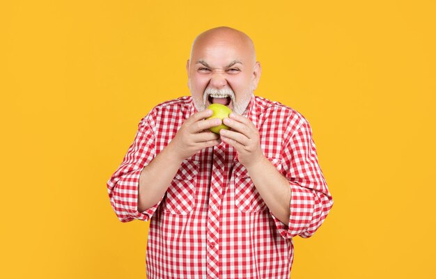 Un anciano hambriento con camisa a cuadros come manzana con fondo amarillo