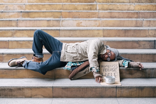 Anciano sin hogar durmiendo en las escaleras de la ciudad