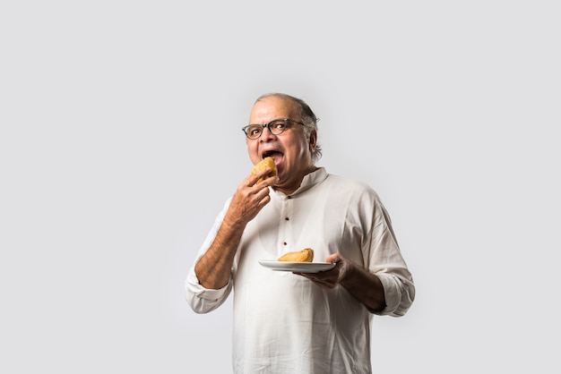 Anciano indio o hombre mayor comiendo samosa o pastelería vegetal
