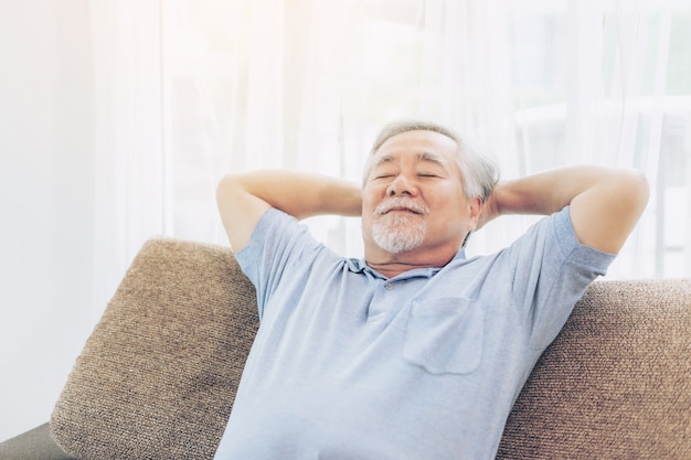 Un anciano jubilado sonriendo, senior hombre relajándose en el sofá de la sala de estar de su casa - concepto de felicidad senior de estilo de vida
