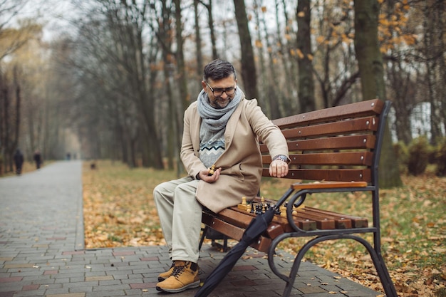 Un anciano juega al ajedrez en un banco en un parque de otoño