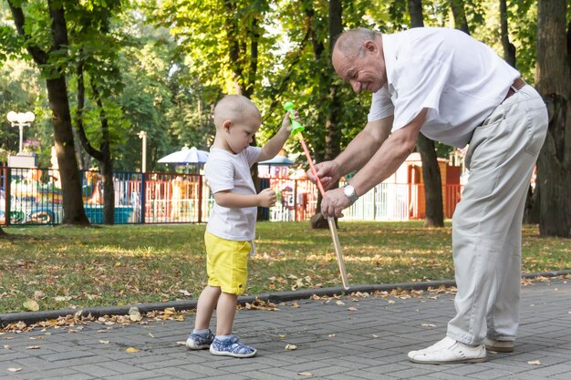 Un anciano juega con su nieto el fin de semana en un parque de diversiones y sopla alegremente pompas de jabón. Un anciano, un jubilado, y un niño pequeño pasan tiempo juntos.