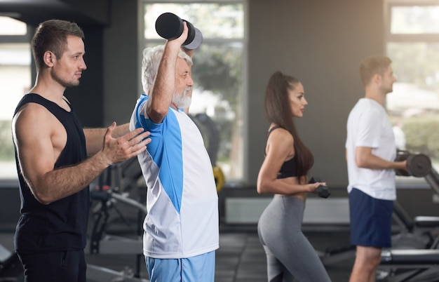 Anciano levantando pesas, entrenador de apoyo.