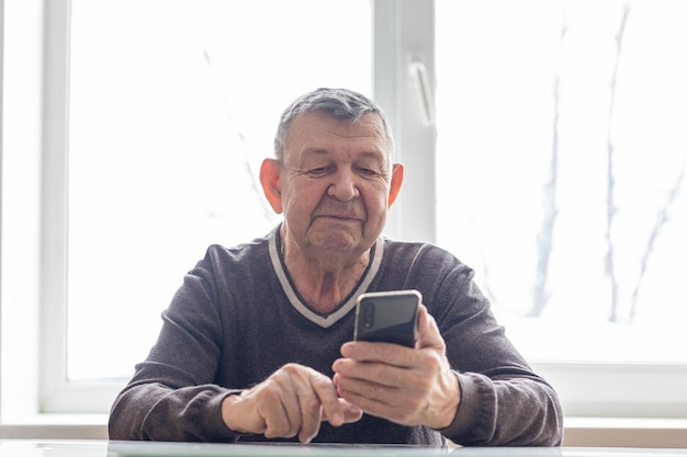 Anciano marca el número en el teléfono inteligente desde casa El anciano envía sms en el teléfono móvil