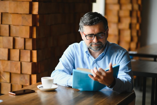 Anciano mayor leyendo un libro en una cafetería disfrutando de su afición literaria