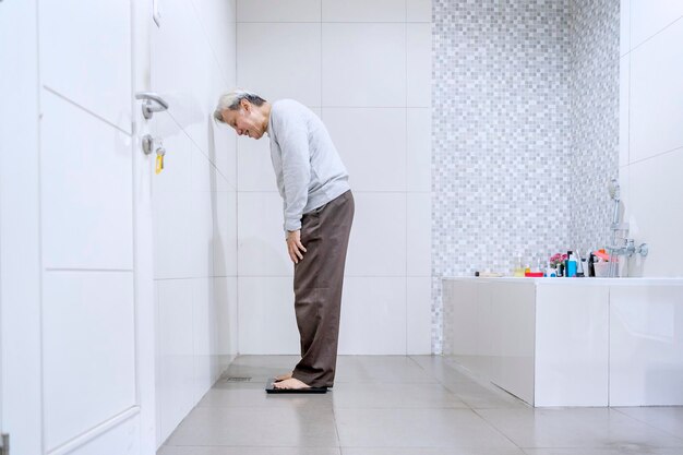 El anciano mide su peso en el baño por la mañana