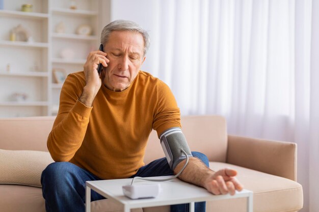 Un anciano midiendo la presión arterial mientras habla por teléfono.