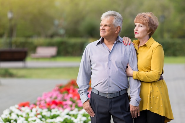 Anciano y mujer de pie en el parque entre flores