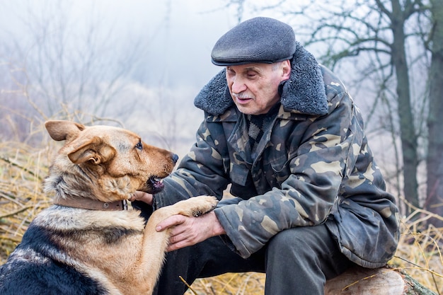 Un anciano en la naturaleza se comunica con un perro. Un hombre y un perro son amigos