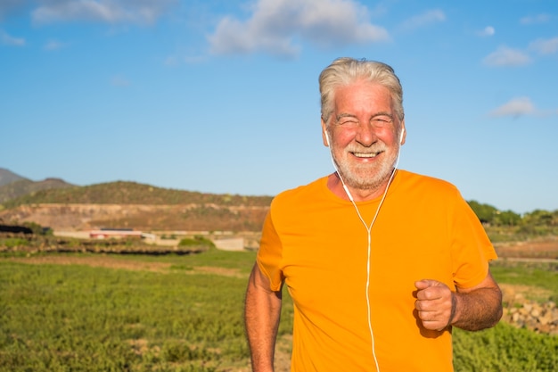Foto anciano o senior corriendo solo en una zona rural alrededor de la naturaleza y las casas - un hombre maduro haciendo ejercicio y perdiendo peso