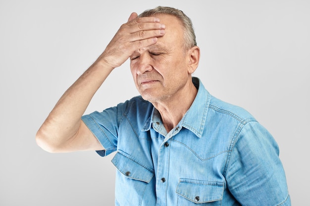 Un anciano de pelo gris con expresión de dolor en la cara se puso la mano en la cabeza, se siente mareado y con dolor de cabeza en racimo, migraña, presión arterial alta o baja aislada en blanco