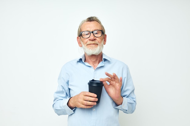 Un anciano de pelo gris gesticula con las manos un vaso de bebida de fondo claro