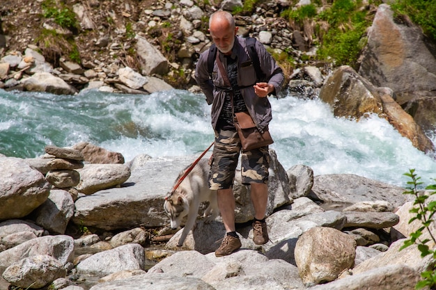 Un anciano y un perro de trineo caminan cerca del río.