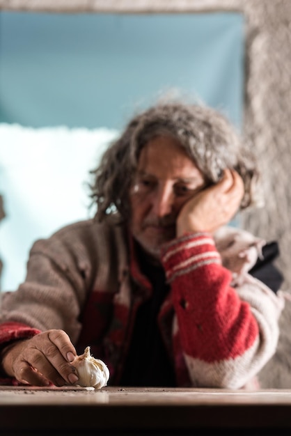 Anciano pobre con las manos sucias sentado sosteniendo un bulbo de ajo