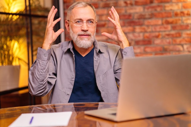 Un anciano preocupado se sienta junto a una computadora portátil e intenta hacer un pago en línea