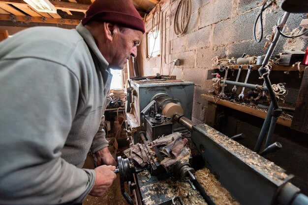 Un anciano procesando madera en un torno y haciendo platos de madera en el taller