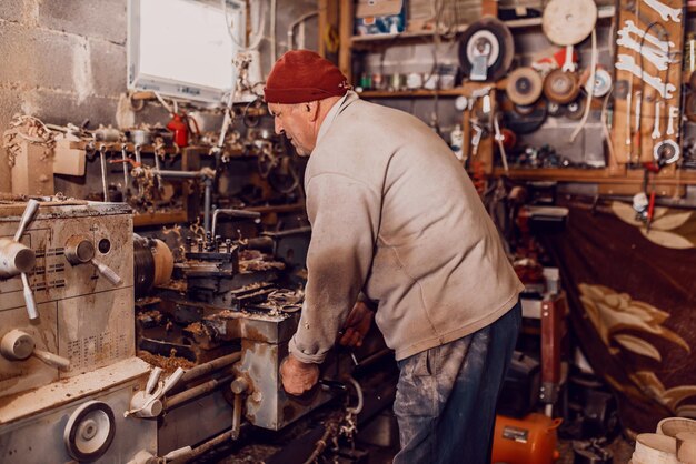 Un anciano procesando madera en un torno y haciendo platos de madera en el taller